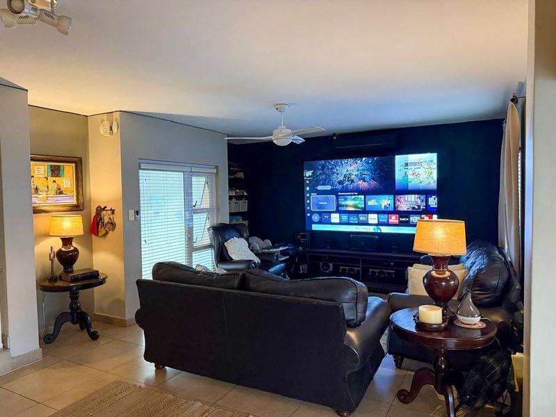 A comfortable living room featuring tiled flooring, a ceiling fan, and an air conditioning unit, with a dedicated media wall setup.