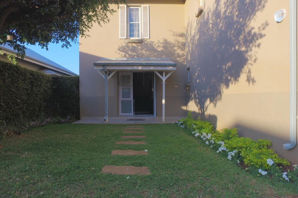 A well-maintained rear garden featuring a covered patio, a stone pathway, and established landscaping against the exterior wall of the house.