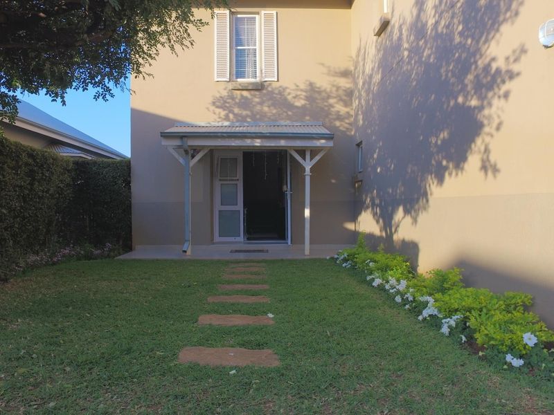 A well-maintained rear garden featuring a covered patio, a stone pathway, and established landscaping against the exterior wall of the house.