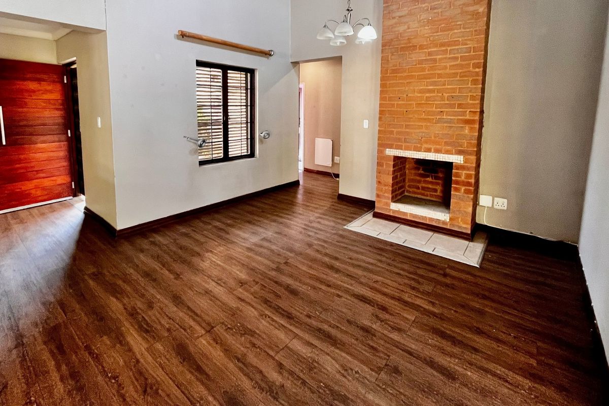 Spacious living room featuring a prominent brick fireplace, dark laminate flooring, and a solid wooden front door.