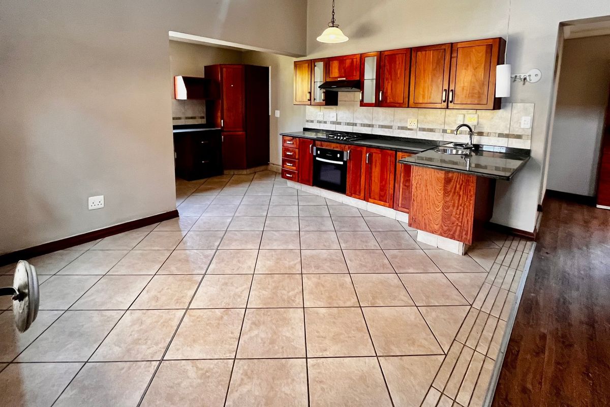 Spacious kitchen featuring wooden cabinetry, granite countertops, built-in oven, gas hob, and tiled flooring, offering a functional layout with an adjacent scullery area.