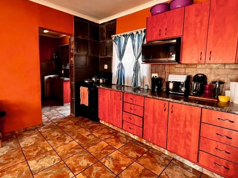 A functional kitchen featuring wood-tone cabinetry, dark tiled backsplash, and tiled flooring, with an adjacent utility area visible through the doorway.