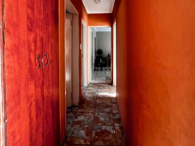 A narrow hallway featuring tiled flooring and a built-in wooden cupboard, providing access to adjacent rooms within the townhouse.