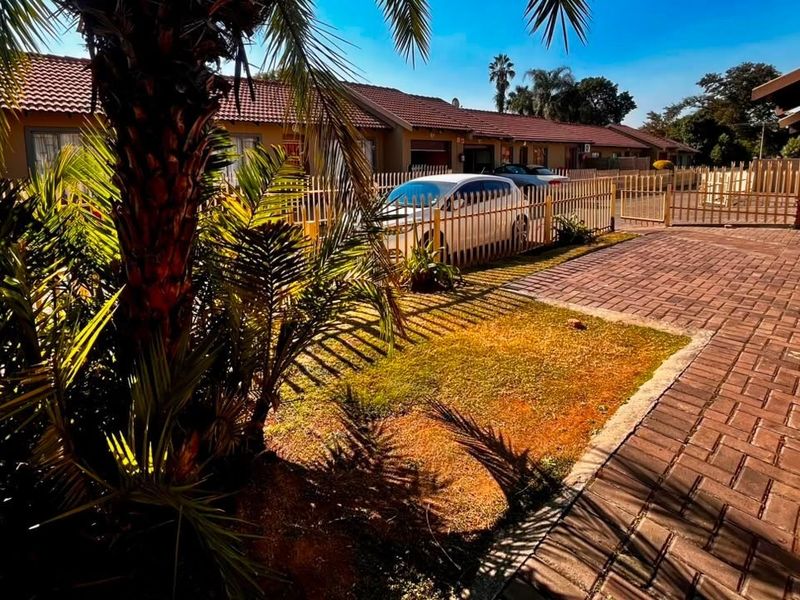 Front exterior view of the townhouse complex featuring a paved driveway, metal fencing, and established garden area.
