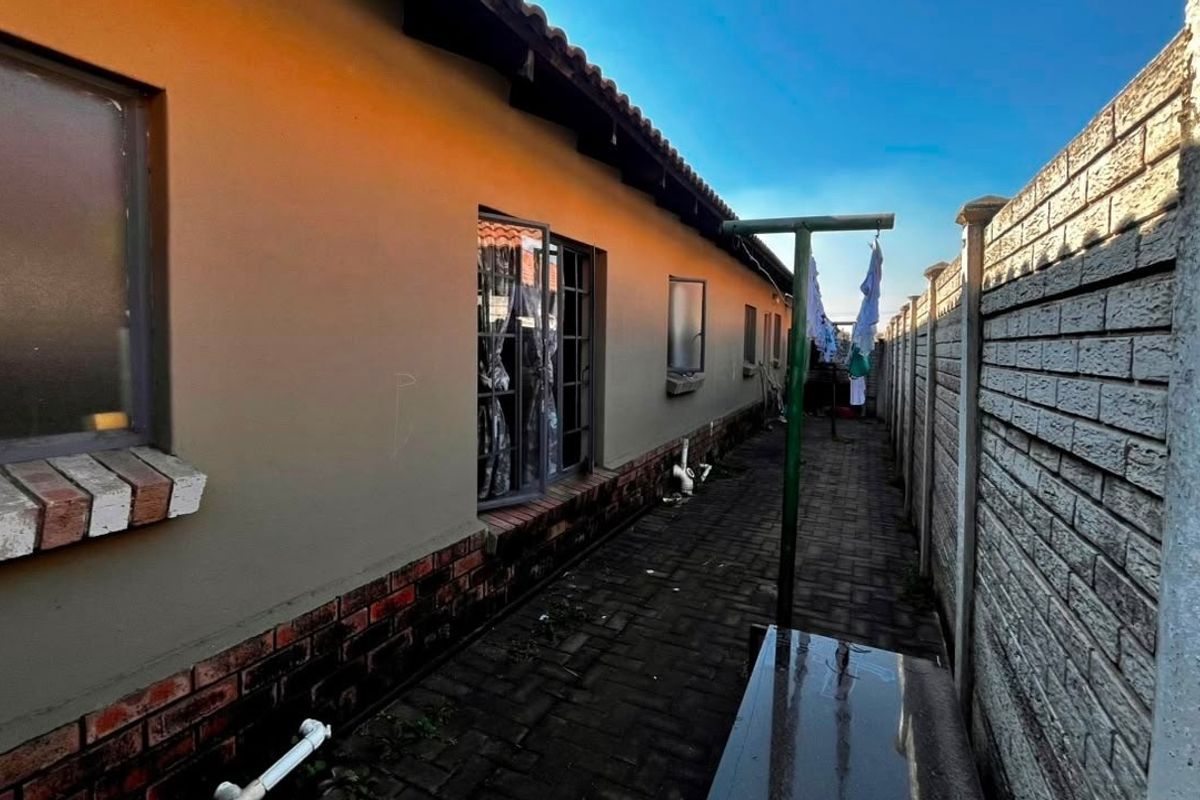 Rear exterior view of the townhouse featuring brick paving, a precast concrete boundary wall, and a tiled roof.