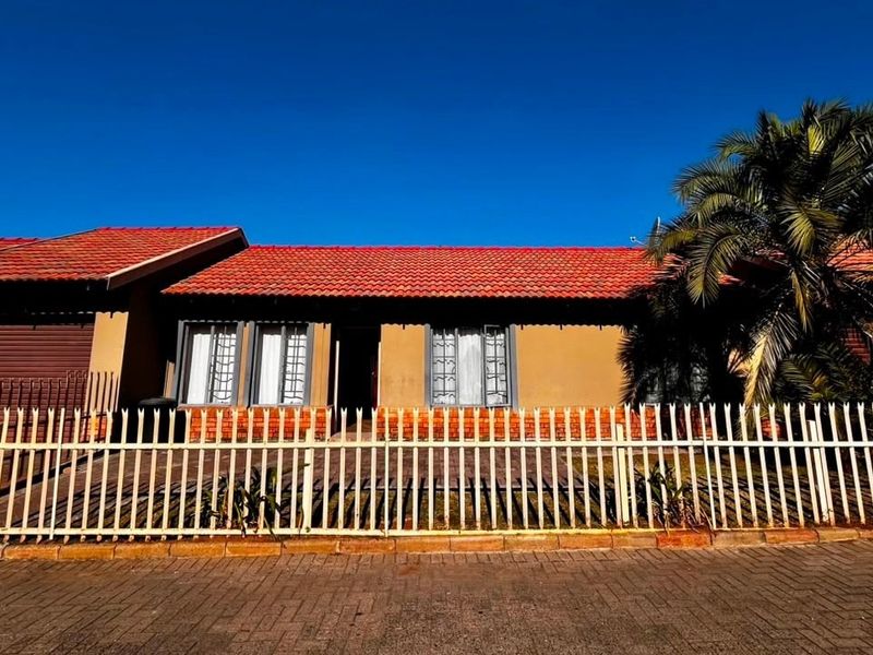 Front elevation of a townhouse featuring a tiled roof, brick facade, secure perimeter fencing, and a paved driveway leading to the garage.