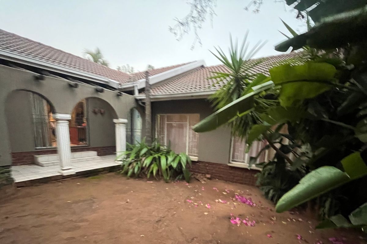 Rear view of the property featuring a covered patio with arched openings, decorative columns, and a tiled roof, overlooking a garden area.