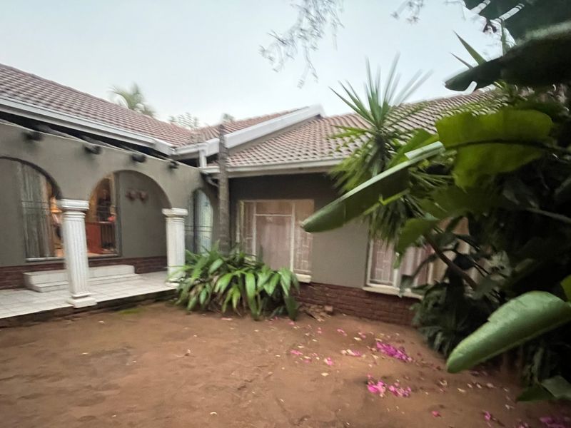 Rear view of the property featuring a covered patio with arched openings, decorative columns, and a tiled roof, overlooking a garden area.