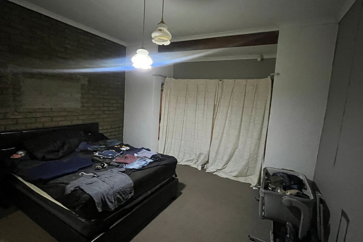 A bedroom featuring an exposed brick feature wall, pendant lighting, and neutral carpeting, requiring cosmetic updates to improve the overall finish.