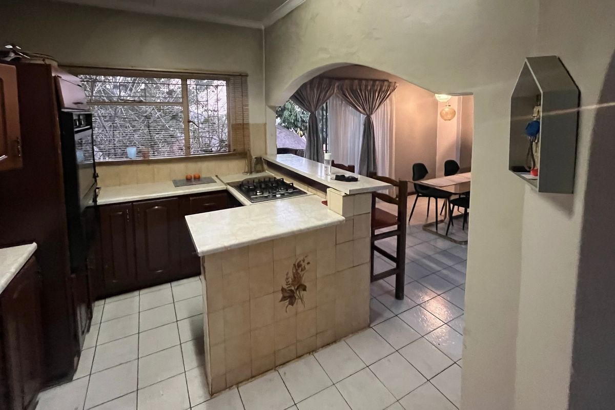 A functional kitchen featuring dark wood cabinetry, a gas hob, and a breakfast bar, opening into the adjacent dining area.