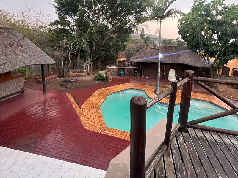Outdoor entertainment area featuring a swimming pool, thatched lapa, built-in braai, and brick-paved patio space.