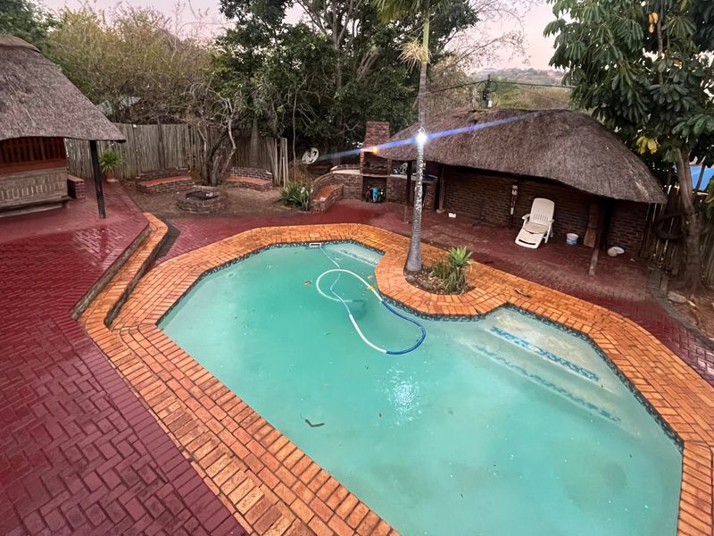 Outdoor entertainment area featuring a swimming pool, two thatch-roofed lapas, and a built-in brick braai, set within a paved garden space.