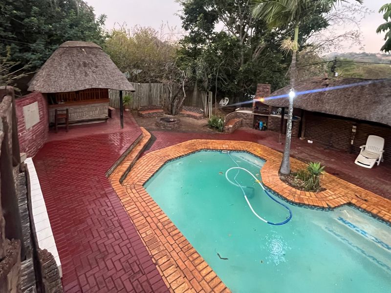 Outdoor entertainment area featuring a swimming pool, two thatched lapas, a built-in braai, and a fire pit set within a landscaped garden.