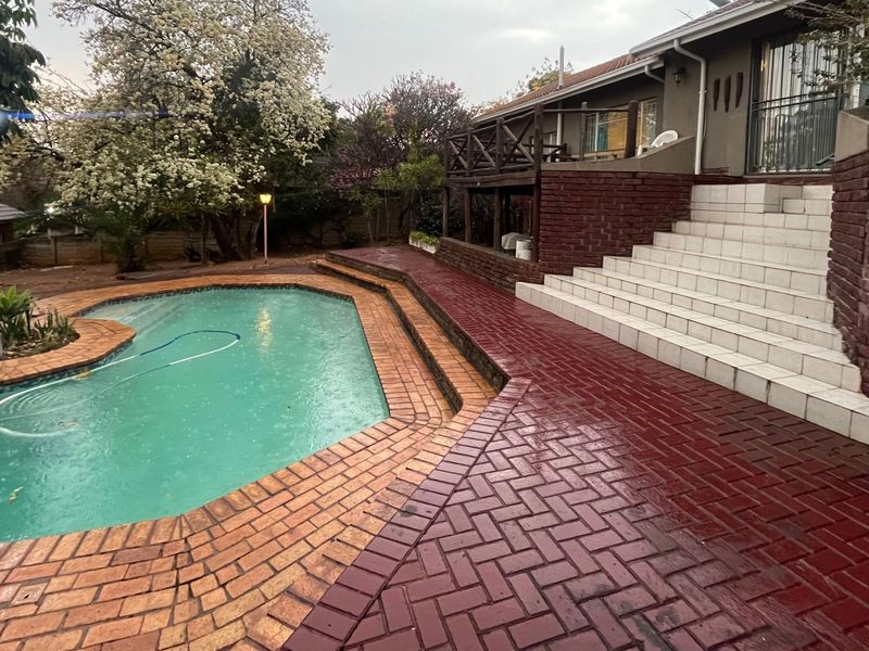 Outdoor pool area featuring a swimming pool, brick paved surround, and a raised wooden deck with tiled stairs leading to the main house.