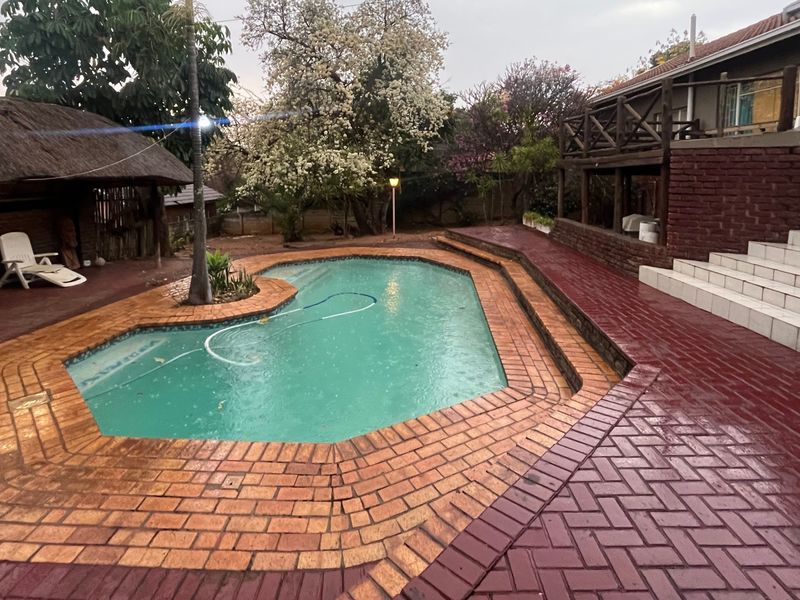 Outdoor pool area featuring a swimming pool, thatched lapa, raised wooden deck, and brick paved surrounds, offering potential for entertainment space enhancement.