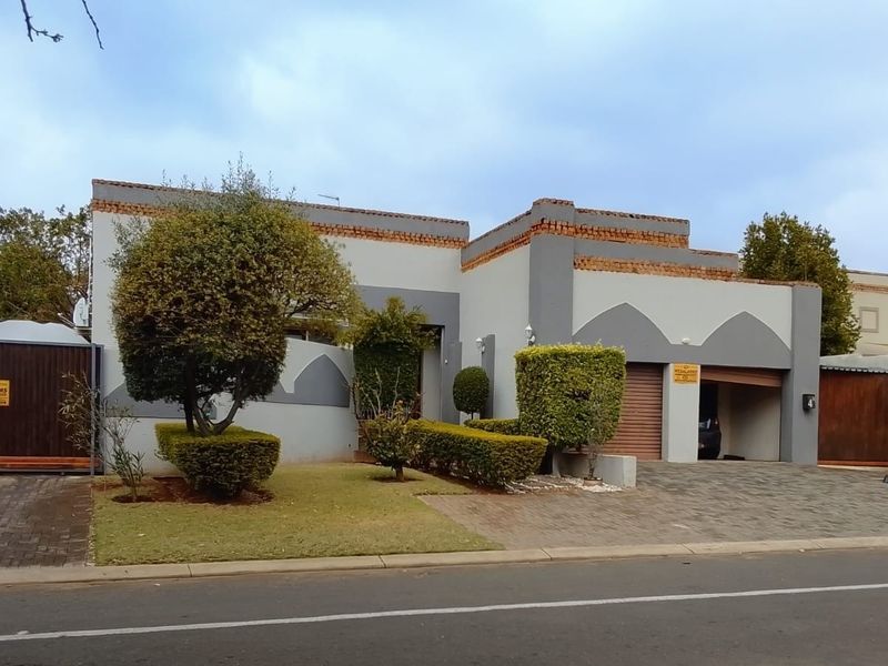 Front elevation of a residential property featuring a paved driveway, integrated garage, and established garden with secure boundary walling and gated access.