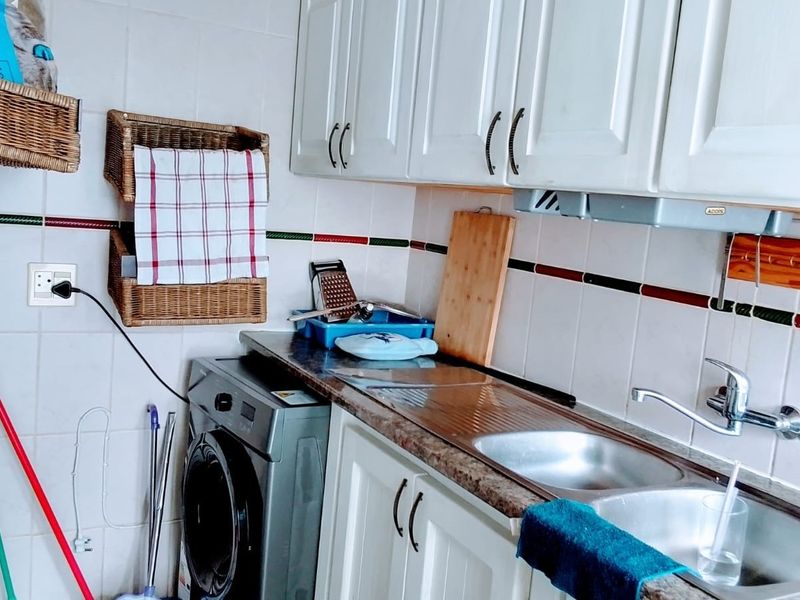 A functional scullery area featuring white cabinetry, a double stainless steel sink, and a tiled backsplash with integrated extractor fan.