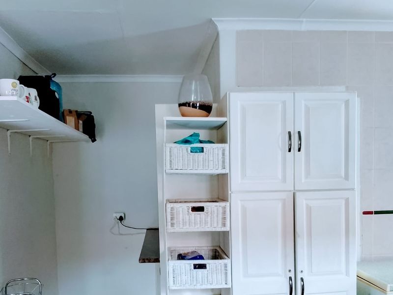 A functional kitchen area featuring white built-in cabinetry, tiled splashbacks, and wall-mounted shelving for storage.