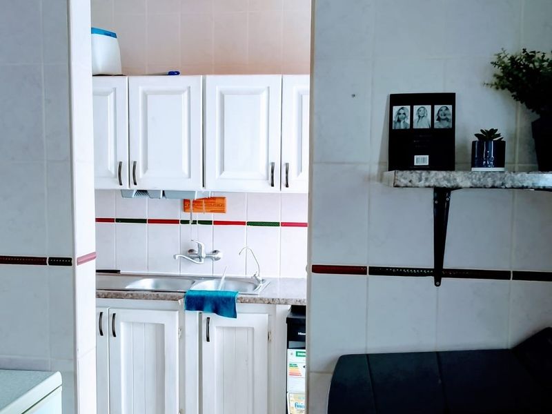 A functional scullery area featuring white built-in cabinetry, a double stainless steel sink, and tiled wall finishes.