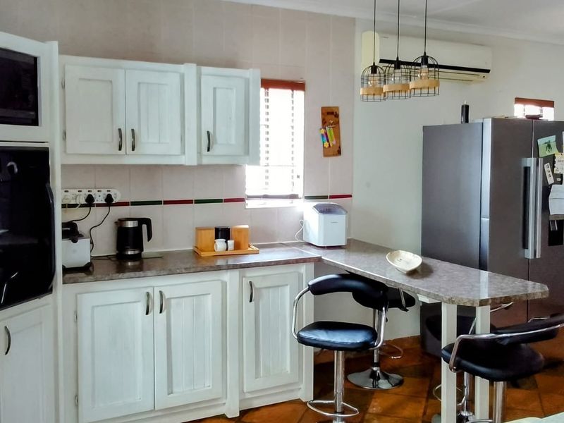 Open-plan kitchen featuring white cabinetry, built-in oven and microwave, laminate countertops, and a breakfast bar, seamlessly flowing into the living area.