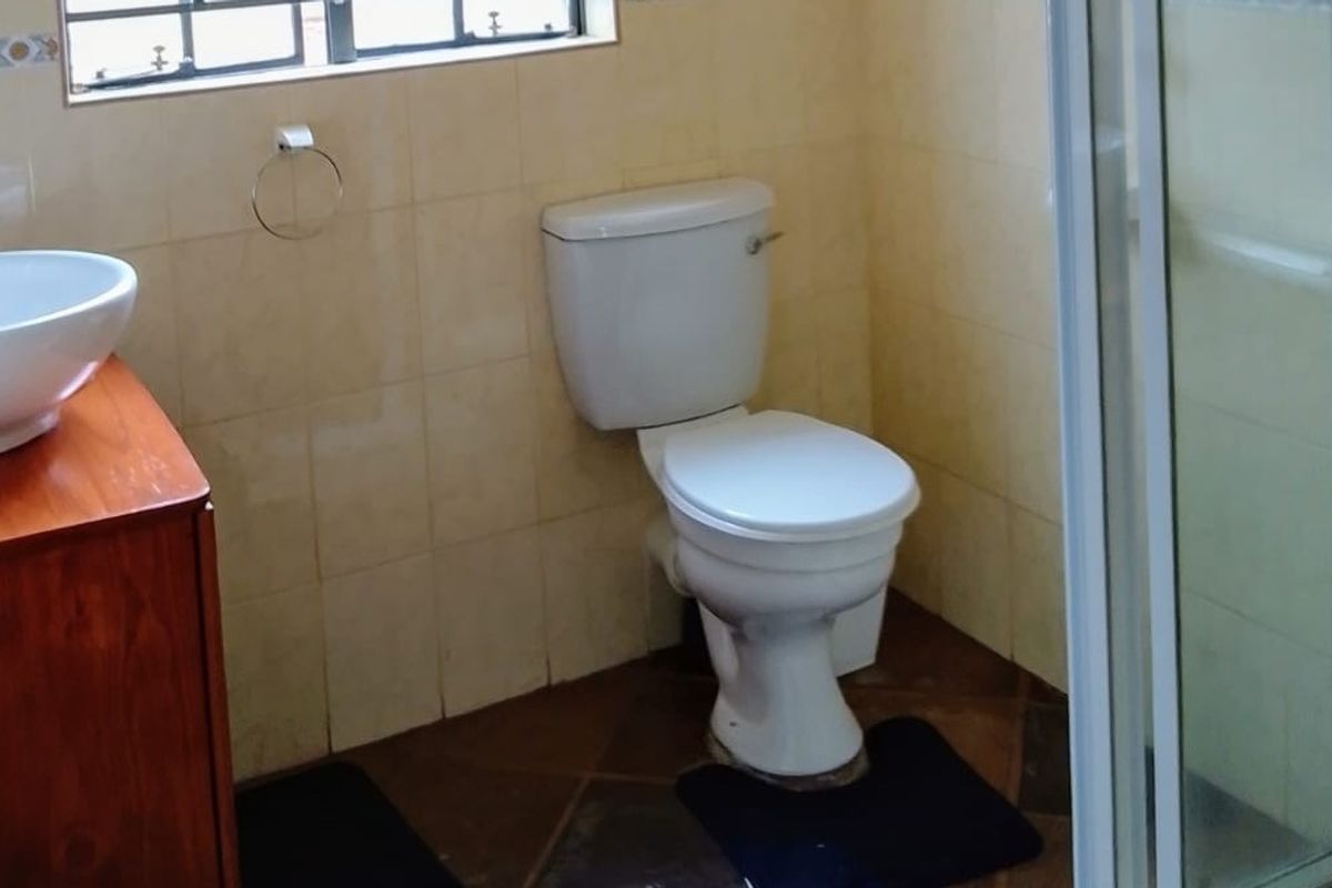 A functional bathroom featuring a vessel sink vanity, standard toilet, and a glass-enclosed shower with tiled walls and flooring.