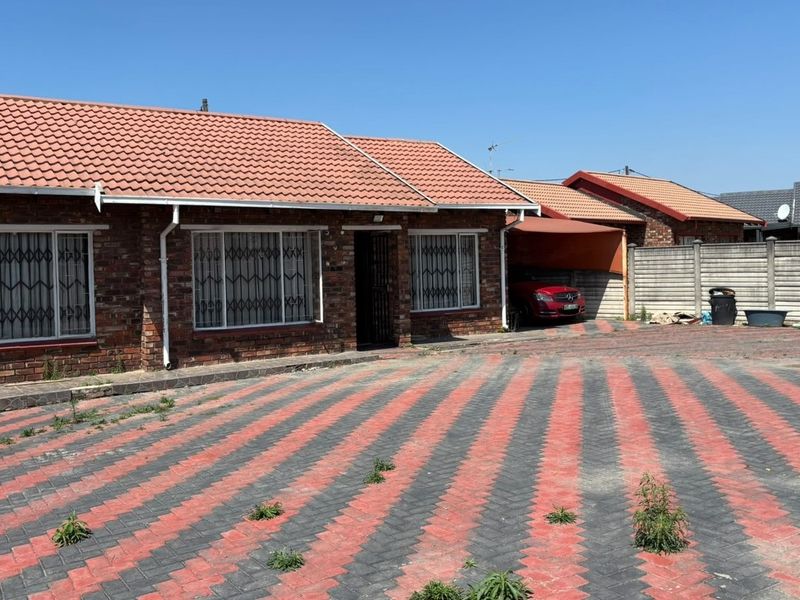 Front exterior view of a face brick house featuring a tiled roof, paved driveway, and a carport, set within a residential property.