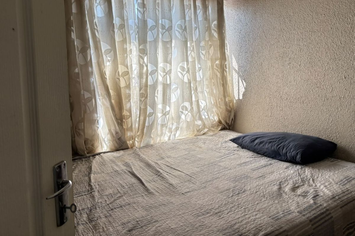 A compact bedroom featuring textured wall finishes and natural light filtering through window curtains.