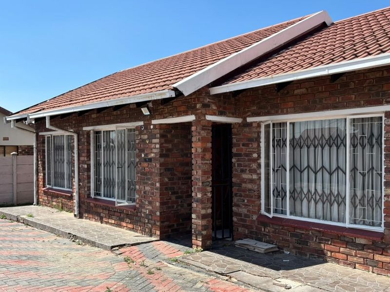 Front exterior view of a face brick house featuring a tiled roof, security gates on windows, and a paved driveway area.
