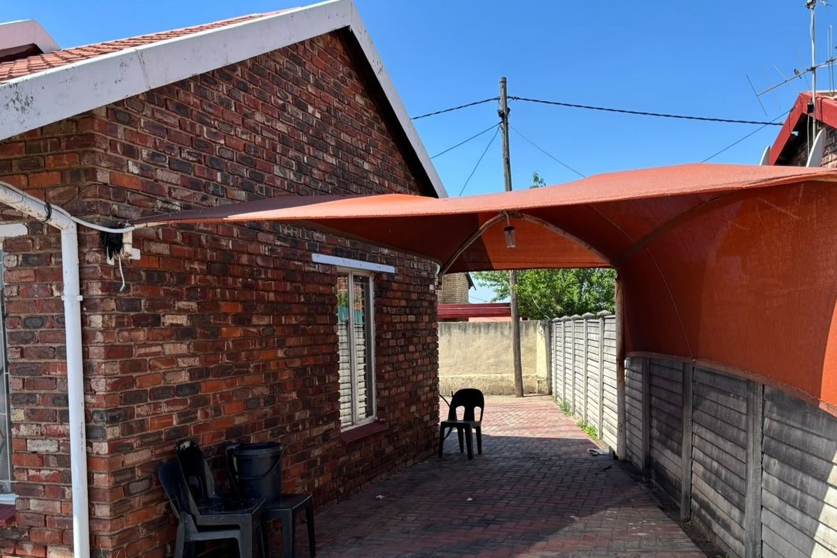 Rear exterior view of a face brick house featuring a paved patio area covered by a shade sail and enclosed by precast concrete boundary walls.