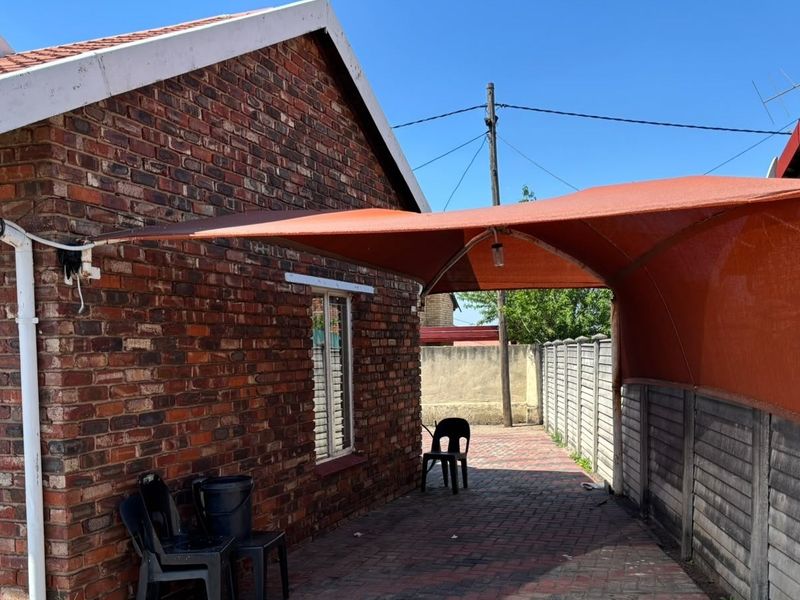 Rear exterior view of a face brick house featuring a paved patio area covered by a shade sail and enclosed by precast concrete boundary walls.
