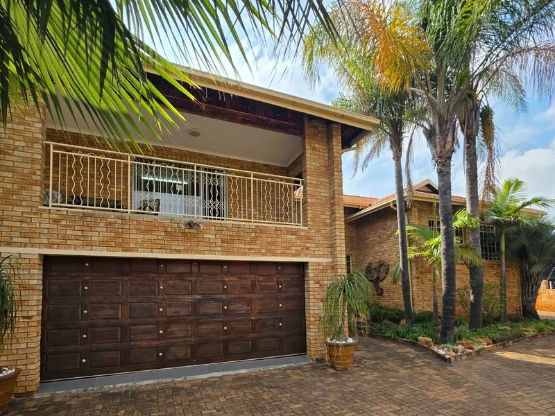 A double-storey face brick residence featuring a timber garage door, a paved driveway, and an upper-level balcony with metal railings.