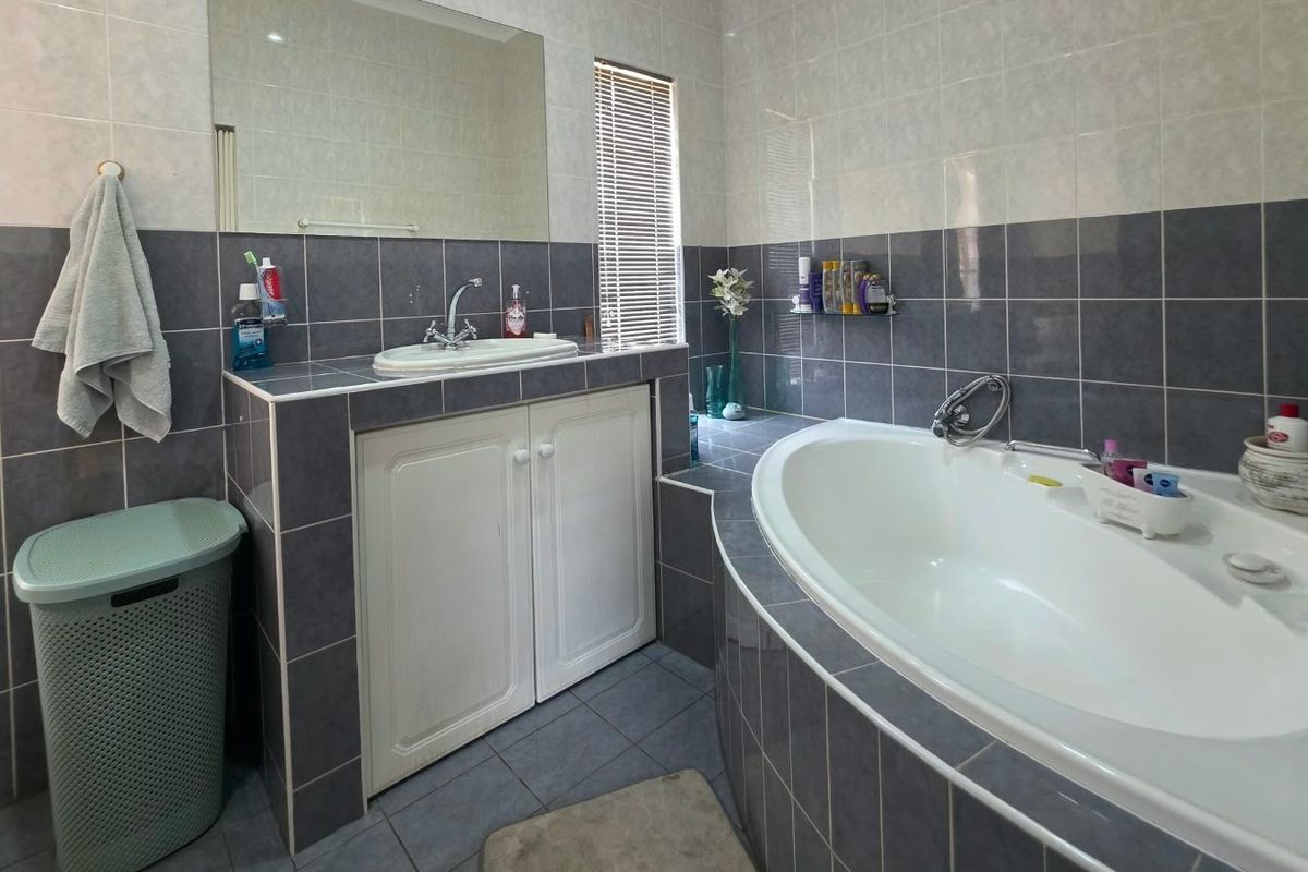 A functional bathroom featuring a built-in bathtub, a tiled vanity area with a drop-in sink, and a large wall mirror.