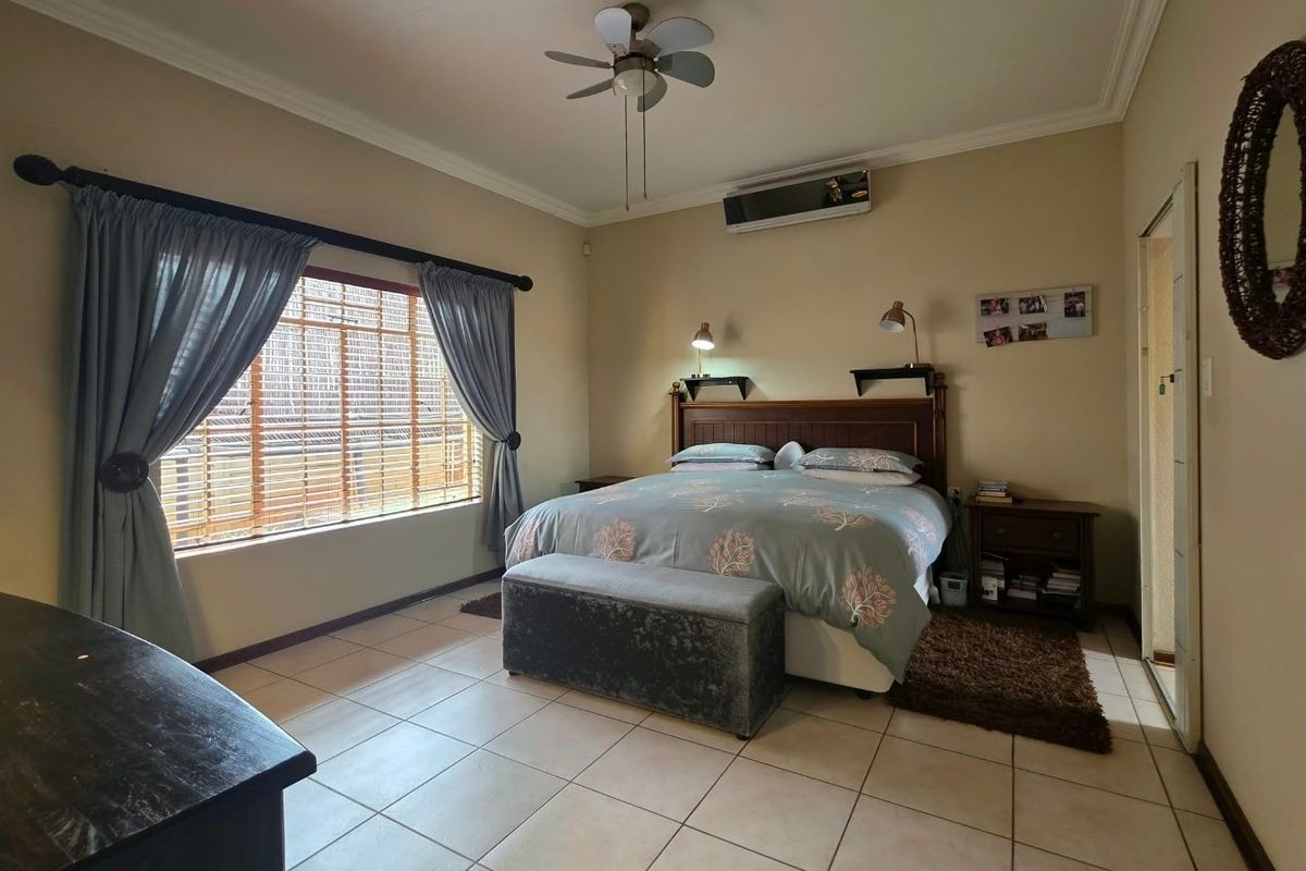 A spacious bedroom featuring tiled flooring, a ceiling fan, and a wall-mounted split-system air conditioner, offering a comfortable and functional living space.