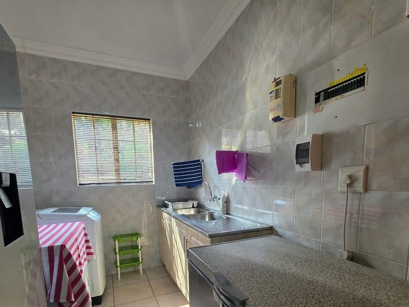 A functional laundry room featuring tiled walls and flooring, a stainless steel sink, and built-in cabinetry with integrated electrical services.