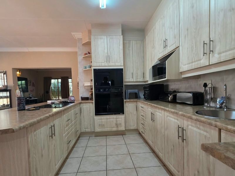A functional kitchen featuring light wood-grain cabinetry, laminate countertops, a double wall oven, and a ceramic hob, with an open-plan layout to the living area.