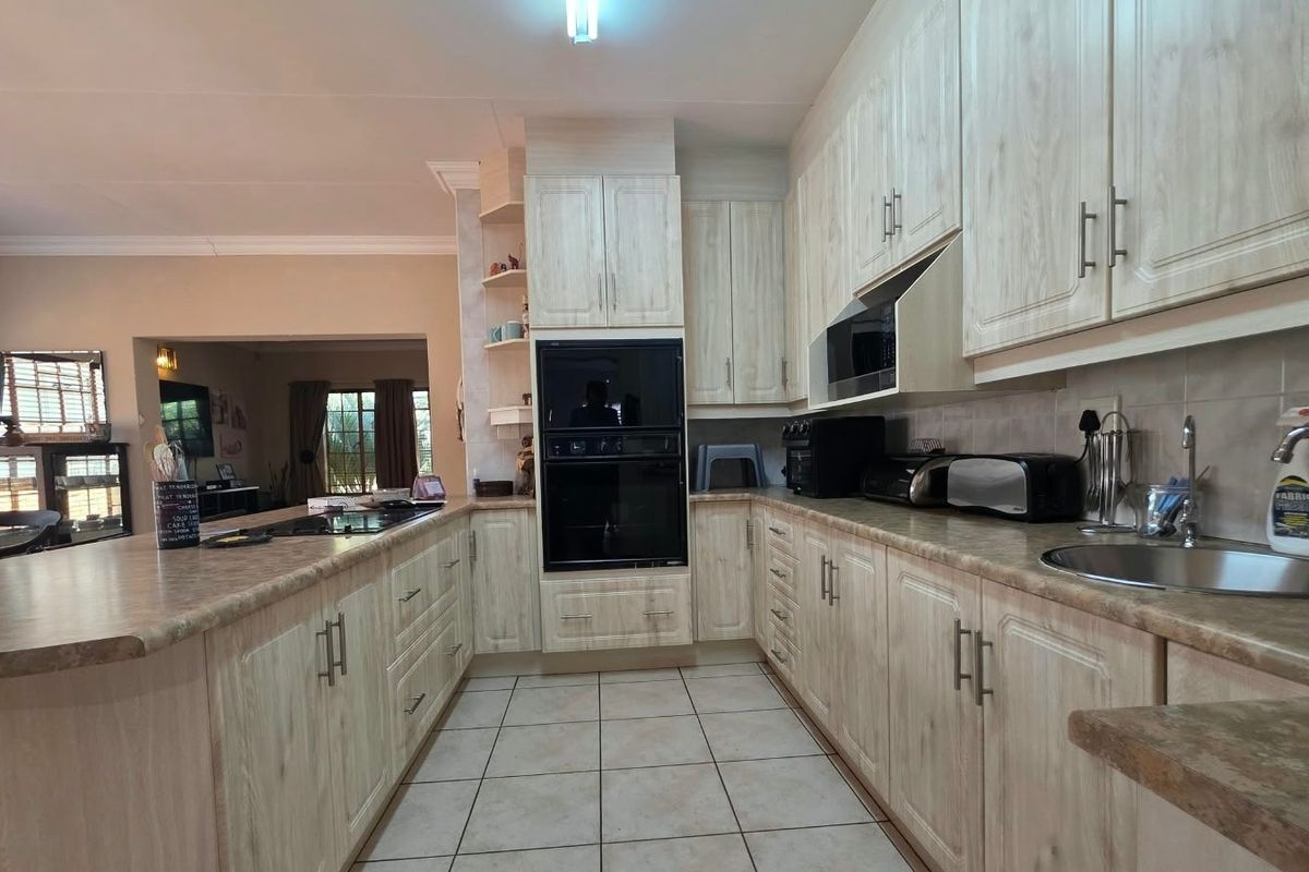 A functional kitchen featuring light wood-grain cabinetry, laminate countertops, a double wall oven, and a ceramic hob, with an open-plan layout to the living area.