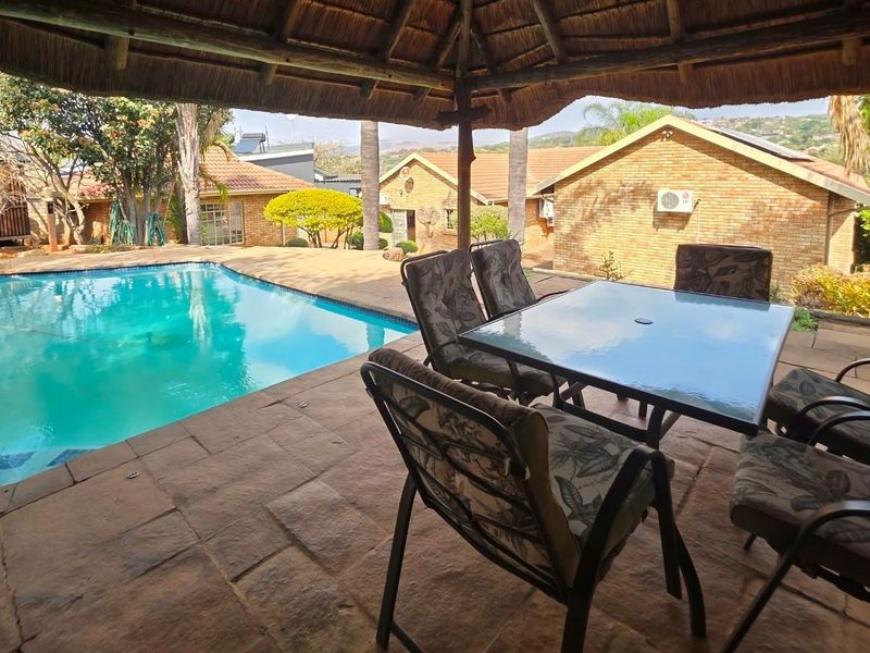 Covered outdoor patio area with a thatched roof overlooking a private swimming pool and landscaped garden.