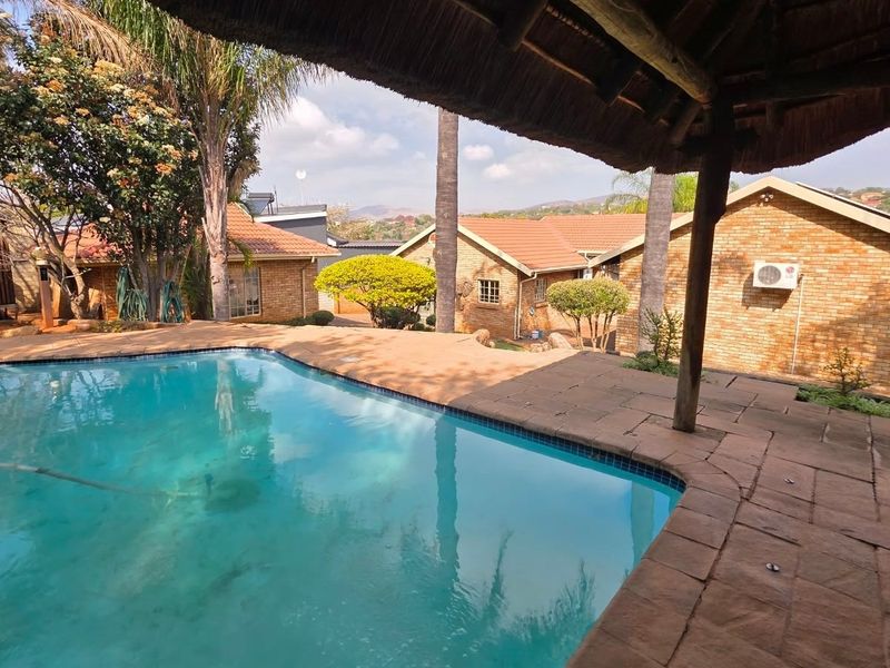Outdoor pool area featuring a paved deck and a covered thatched patio, overlooking the surrounding brick residential structures.
