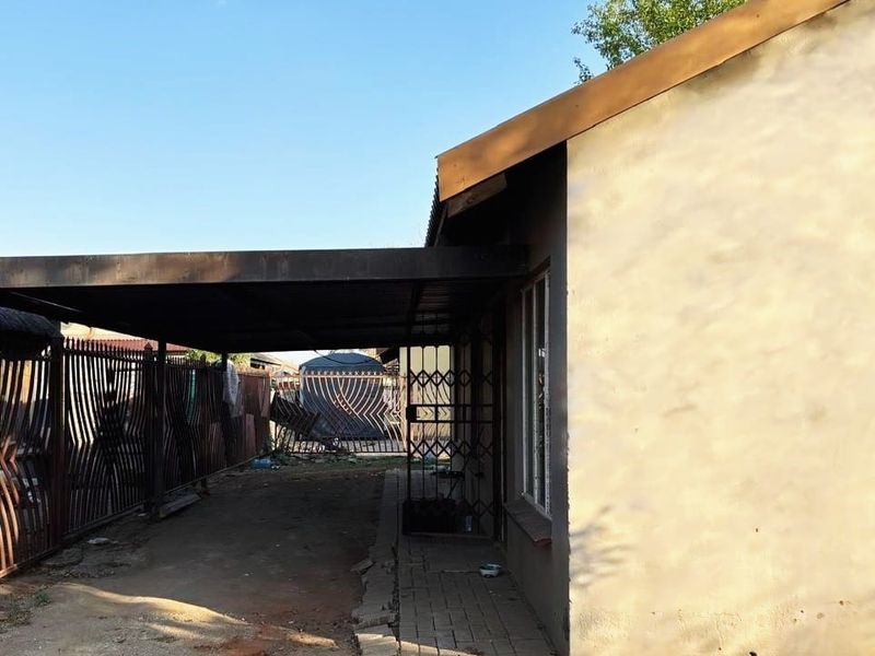 Side view of the property featuring a metal carport, security gate, and paved walkway along the exterior wall.