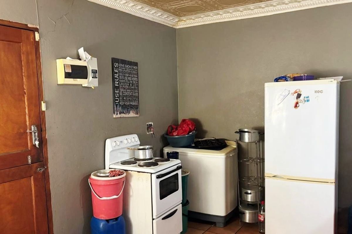 A functional kitchen area featuring a freestanding stove, tiled flooring, and decorative ceiling cornicing, requiring cosmetic updates to improve its overall condition.