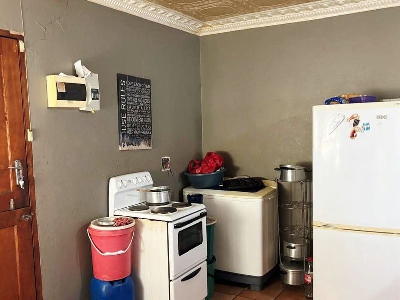 A functional kitchen area featuring a freestanding stove, tiled flooring, and decorative ceiling cornicing, requiring cosmetic updates to improve its overall condition.