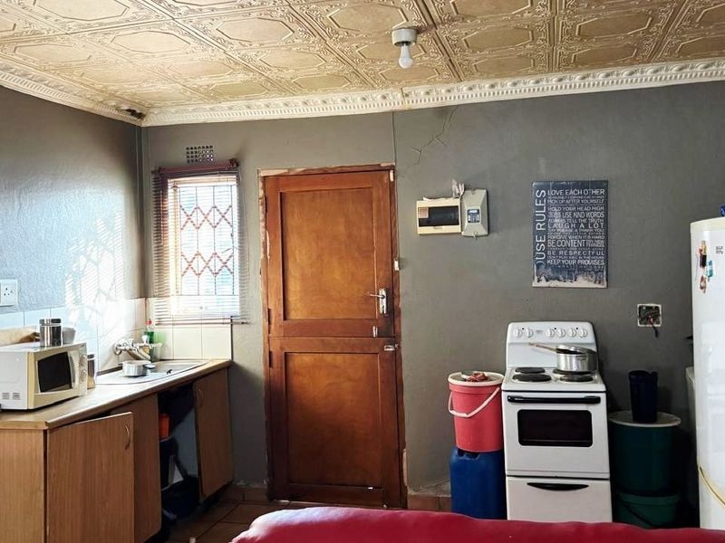 A dated kitchen featuring decorative ceiling tiles, built-in cabinetry, and a freestanding stove, requiring cosmetic updates and repairs to wall finishes.