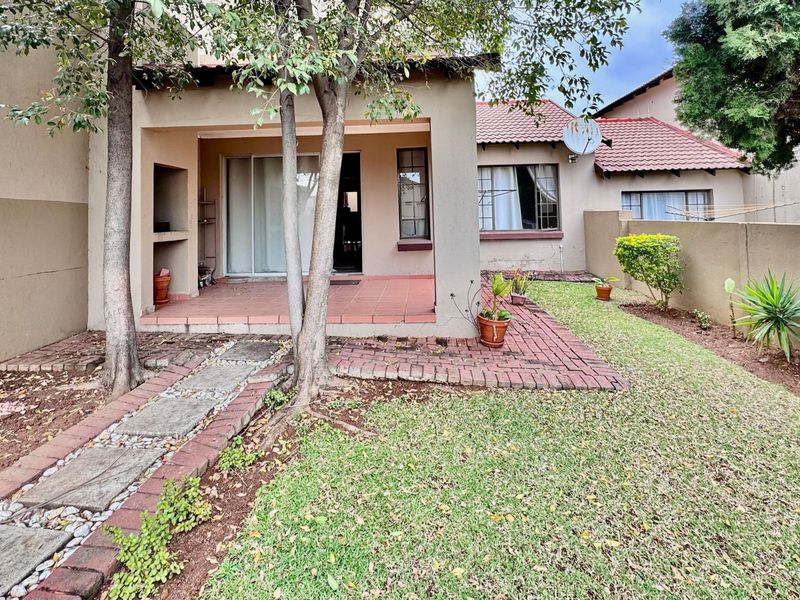 Rear view of the townhouse featuring a covered patio with a built-in braai, brick-paved walkway, and a private garden area.