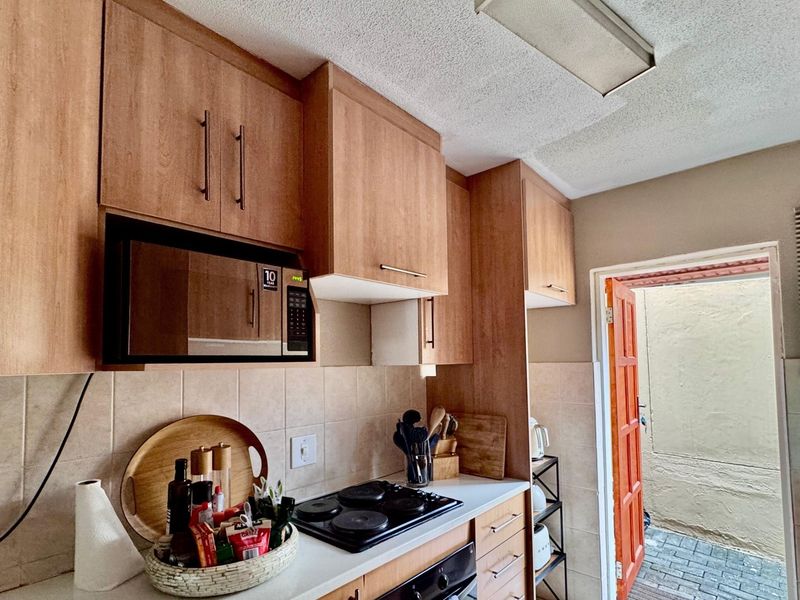 Compact kitchen featuring wood-look cabinetry, built-in oven and hob, tiled backsplash, and direct access to an outdoor paved area.