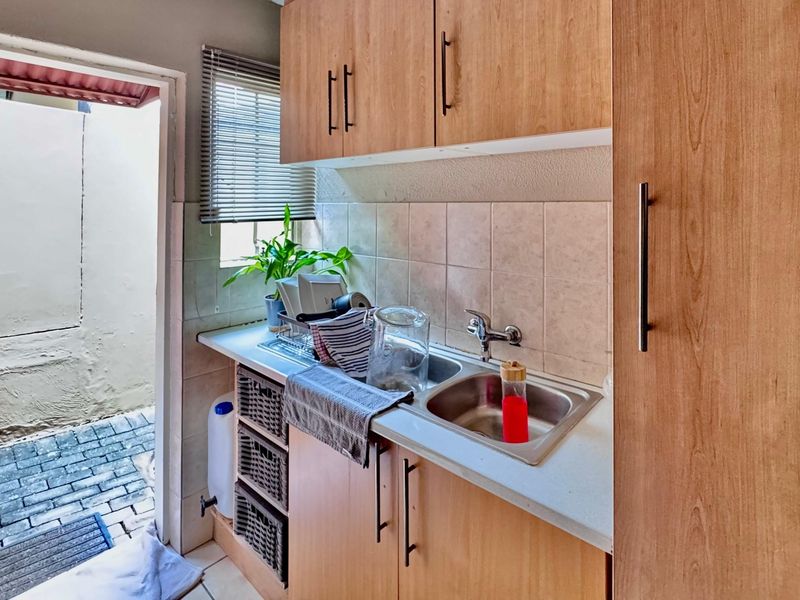 Compact scullery area featuring laminate cabinetry, a double stainless steel sink, and direct access to an outdoor paved courtyard.