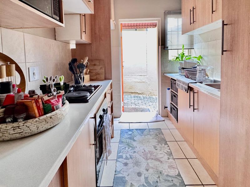 A functional galley-style kitchen featuring light wood-finish cabinetry, built-in appliances, tiled backsplash, and direct access to an outdoor area.