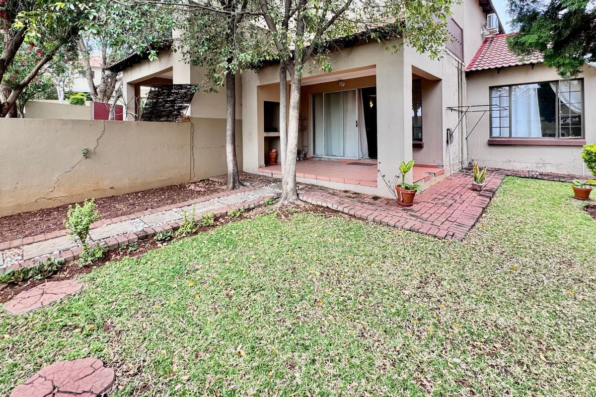 Rear view of the townhouse featuring a covered patio with a built-in braai, brick paving, and a private garden area.