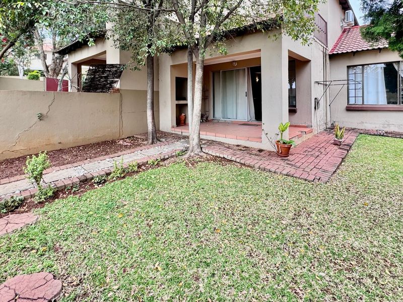 Rear view of the townhouse featuring a covered patio with a built-in braai, brick paving, and a private garden area.
