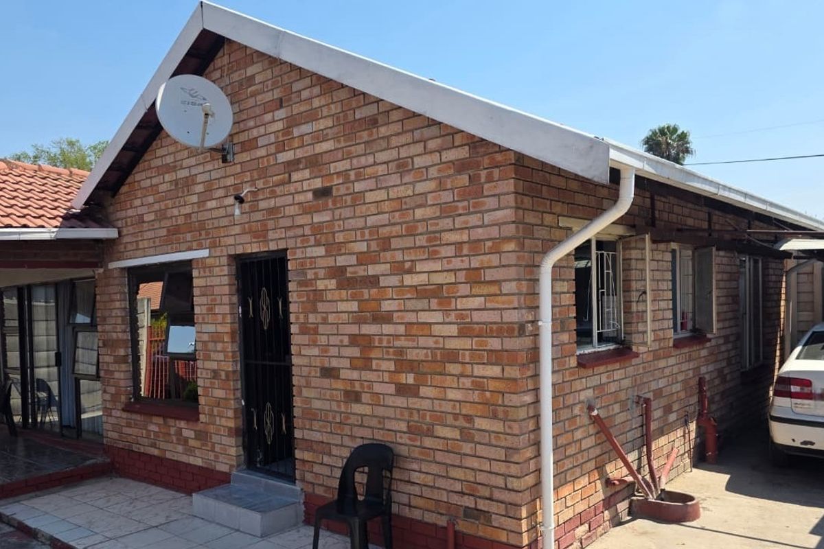 Rear view of a face brick house featuring a tiled roof, security gates, and burglar bars on windows.