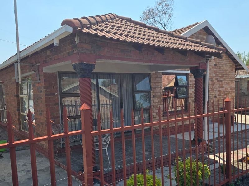 A face brick residential property featuring a covered front patio with decorative columns and secure metal perimeter fencing.